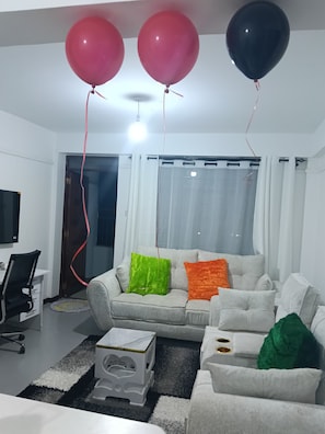 A living room with a grey sofa, colorful cushions, a white coffee table, and three balloons tied to the ceiling. - Cozy 1-bedroom apartment in lovely Nanyuki with AC.Mt Kenya view, Olpejeta Conse (Nanyuki)