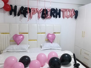 Ein Schlafzimmer mit einem Bett, Kissen und einer Wanddekoration mit Ballons, die ‚HAPPY BIRTHDAY‘ buchstabieren.