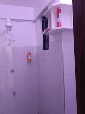 A bathroom with white tiled walls, a shower, a hairdryer, and a shelf with a red bottle. - Cozy 1-bedroom apartment in lovely Nanyuki with AC.Mt Kenya view, Olpejeta Conse (Nanyuki)