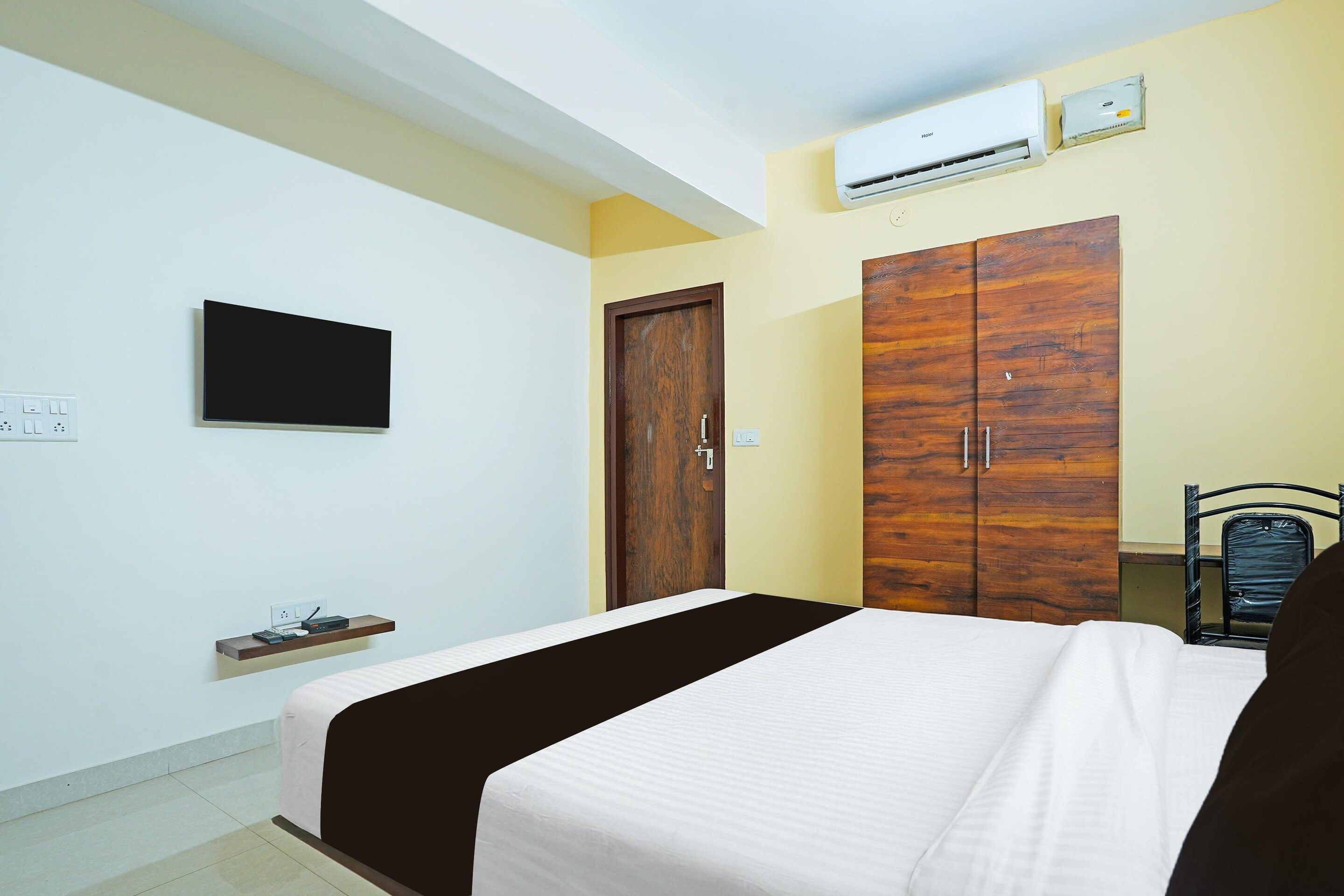 A bedroom with a bed, a wardrobe, a television, and an air conditioning unit.