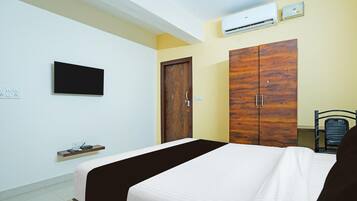 A bedroom with a bed, a wardrobe, a television, and an air conditioning unit.