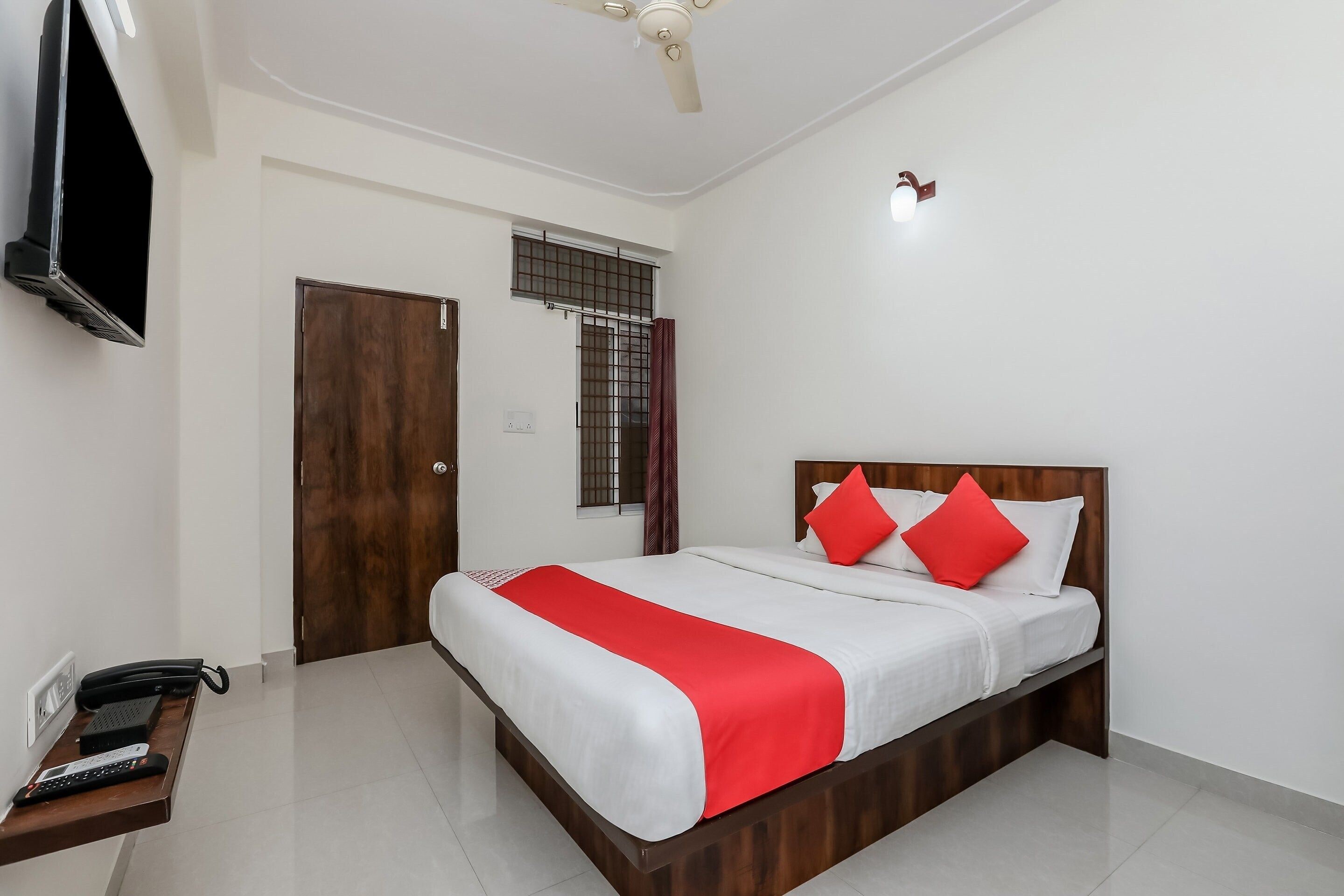 A hotel room with a bed, a desk with a telephone, and a television mounted on the wall.