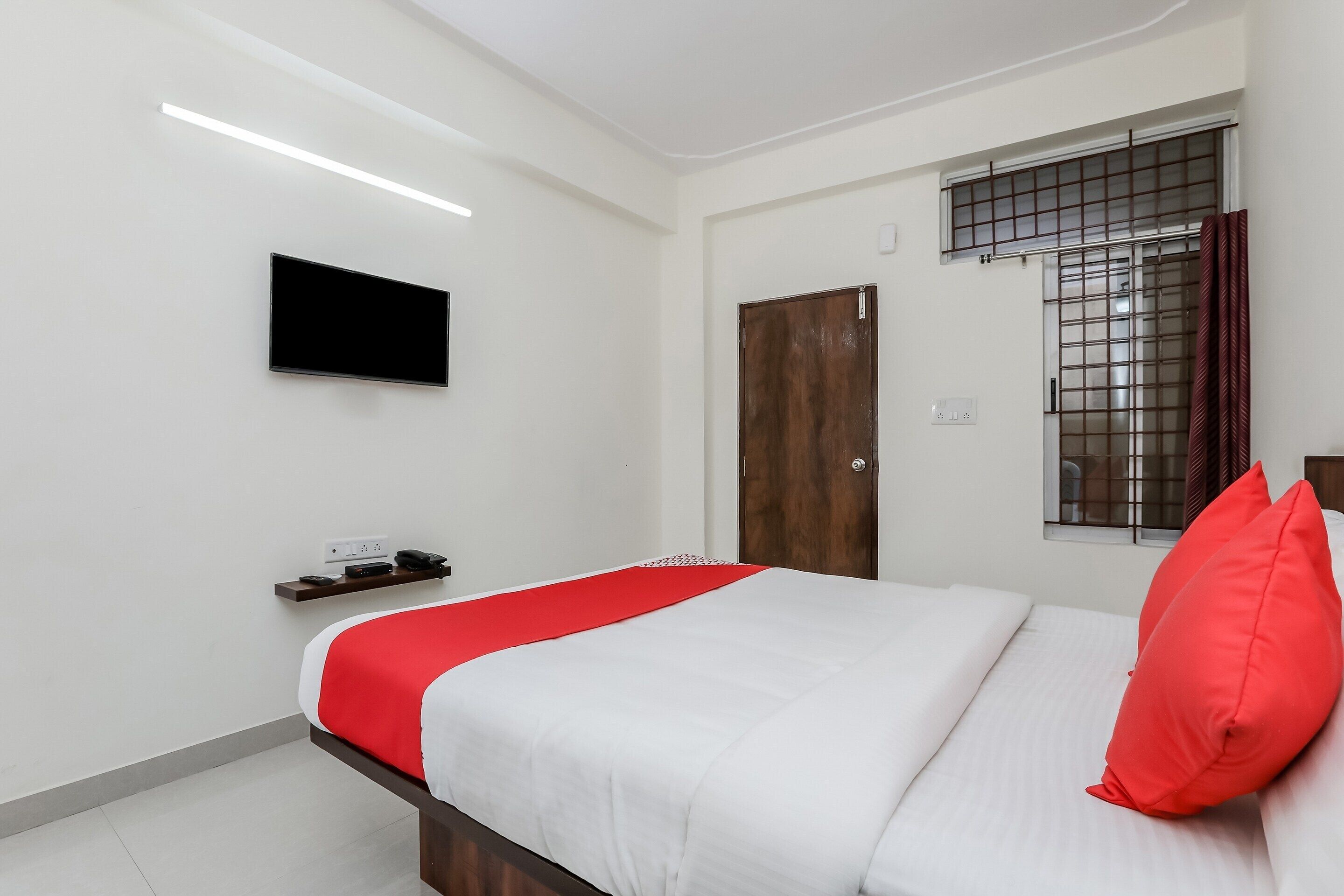 Une chambre à coucher avec un lit, un téléviseur fixé au mur, une fenêtre avec une grille en métal et une porte.