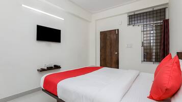 Une chambre à coucher avec un lit, un téléviseur fixé au mur, une fenêtre avec une grille en métal et une porte.