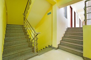 A staircase with a fire exit sign, leading to a landing with windows and a door.