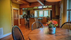 A wooden dining table with chairs, a potted plant, and a kitchen in the background. - The Retreat - Luxury Mountain Home (Roseland)