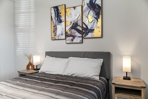 A bedroom with a bed, two bedside lamps, and three abstract paintings on the wall. - Waterfront 4-bedroom luxury pool home (Winter Haven)