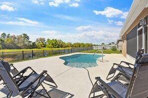 A swimming pool with a curved edge, surrounded by a concrete deck and metal chairs. - Waterfront 4-bedroom luxury pool home (Winter Haven)