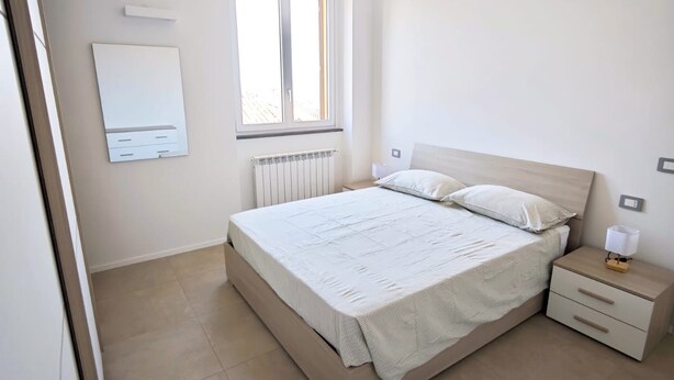 Quarto com cama, mesa de cabeceira, janela e radiador.