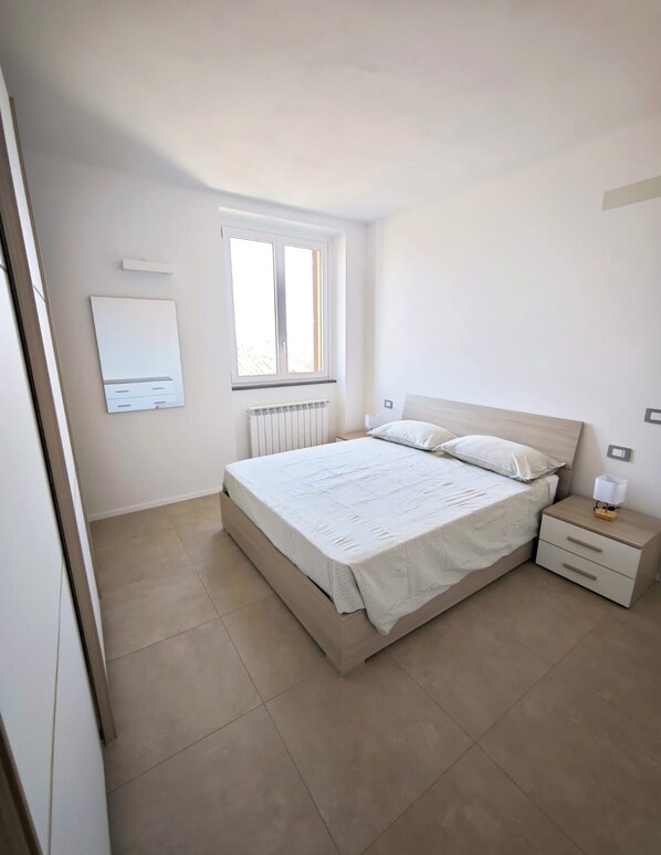 Ein Schlafzimmer mit einem Bett, einem Nachttisch, einem Fenster und einer Heizung.