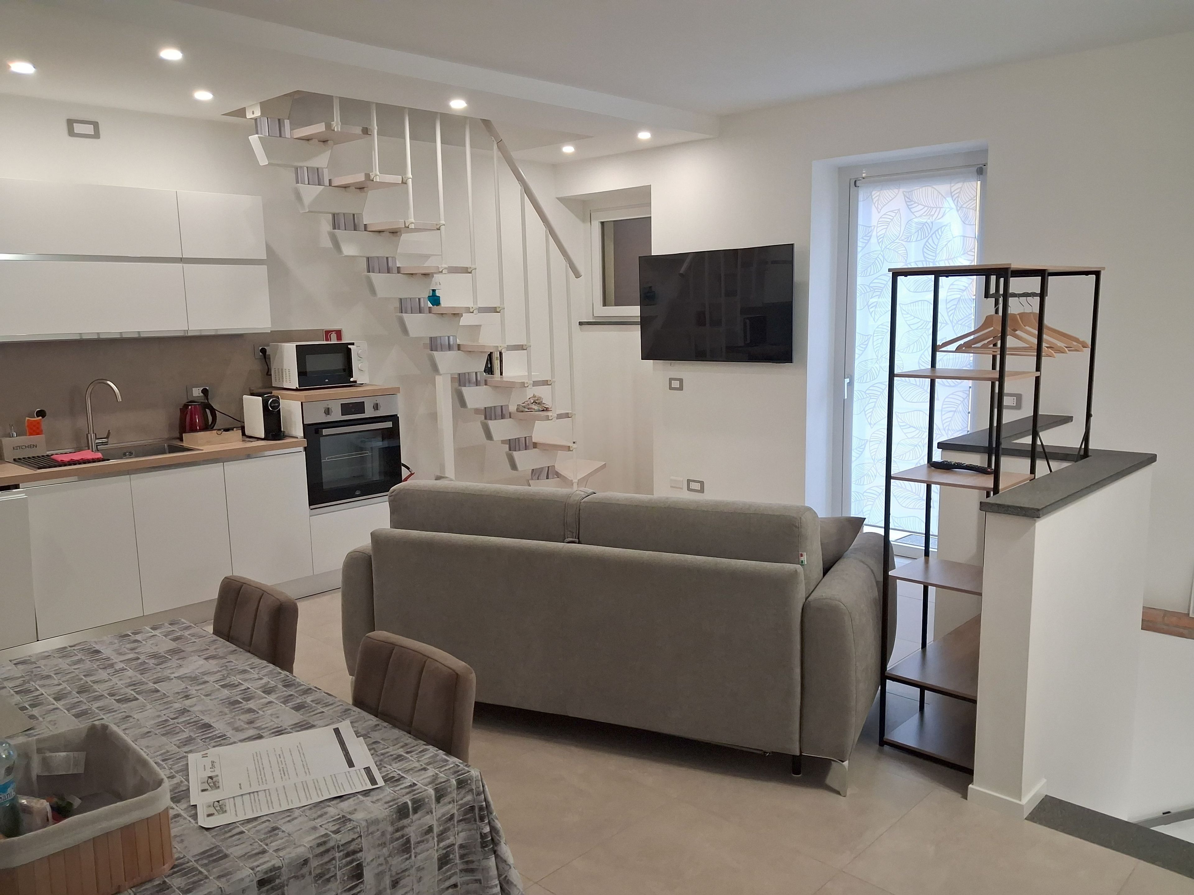 Eine moderne Küche mit Backofen, ein Essbereich mit Tisch und Stühlen, eine Sitzecke und eine Treppe mit an der Wand montiertem Fernseher.