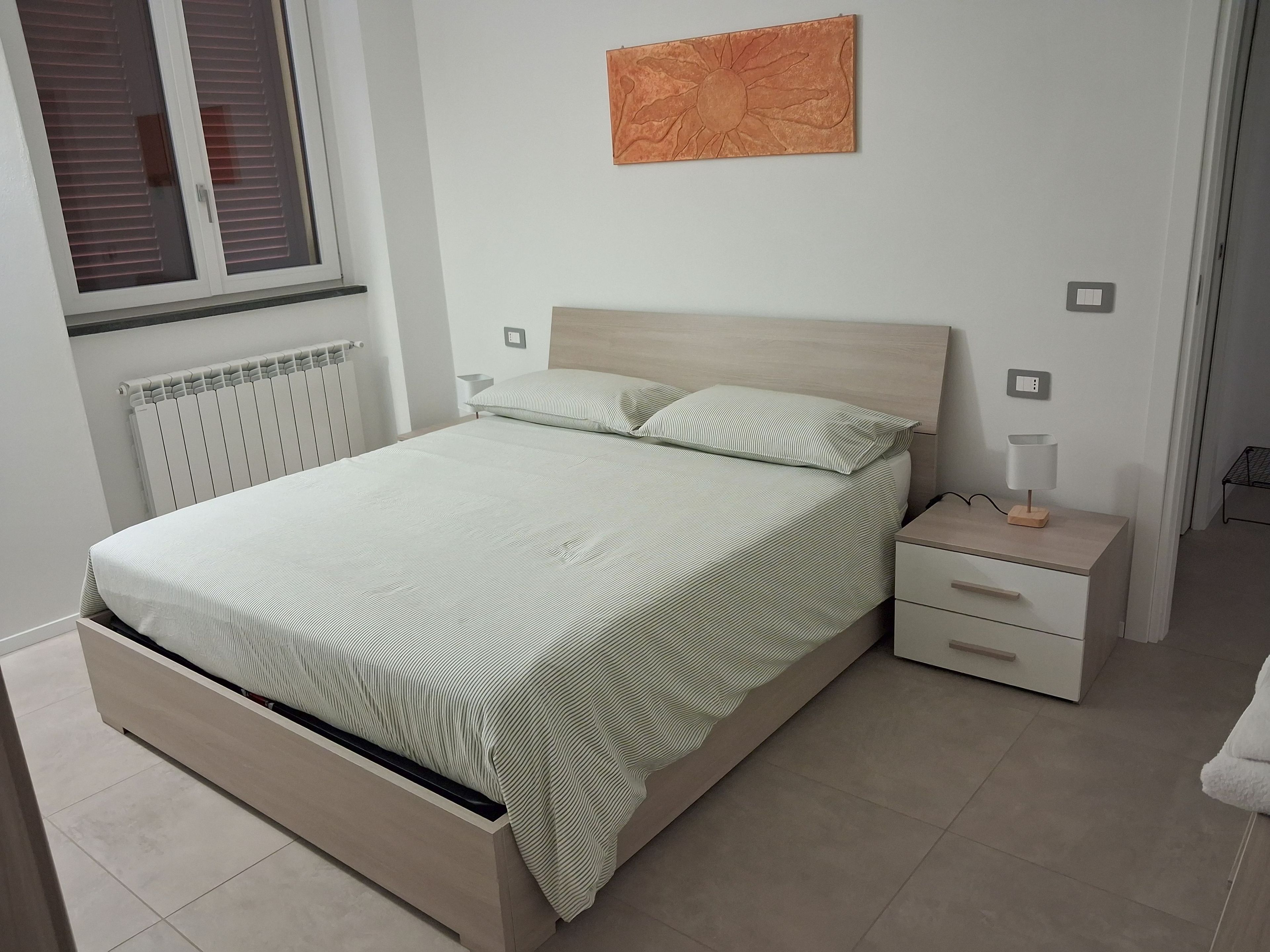 Une chambre à coucher comprenant un lit, une table de chevet, une lampe et une œuvre d’art accrochée au mur.