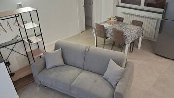 Ein Wohnzimmer mit grauem Sofa, einem kleinen Tisch mit Stühlen und einer Heizung.