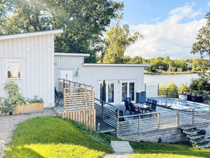 Uma cabana branca com terraço e área de estar ao ar livre com vista para um lago.