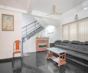 Una sala de estar moderna con un sofá de cuero negro, una mesa de centro de vidrio, una silla de metal, una escalera y un ventilador de techo.