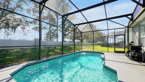 Una piscina con superficie d'acqua cristallina e azzurra, circondata da una veranda coperta con barbecue e mobili da esterno.
