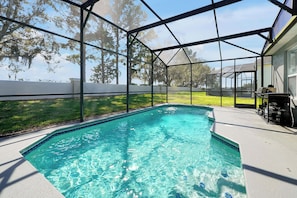 Una piscina con superficie de agua azul cristalina, rodeada por un porche cubierto con una parrilla y mobiliario exterior.