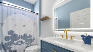 Un bagno con tenda da doccia raffigurante un personaggio dei cartoni animati, un water, un lavandino con rubinetti dorati e uno specchio sopra il lavandino.