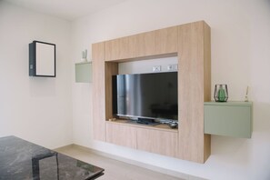 A modern living room with a flat-screen TV mounted on a wooden wall unit, a small table, and a green cabinet with decorative items. - Aetnamare: A 360° View (Mascalucia)