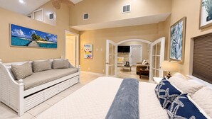 A bedroom with a large bed, a sofa, and a view of a living area. - The Canal Cottage (Fort Myers)