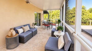 A covered outdoor seating area with sofas, a table, and chairs. - The Canal Cottage (Fort Myers)