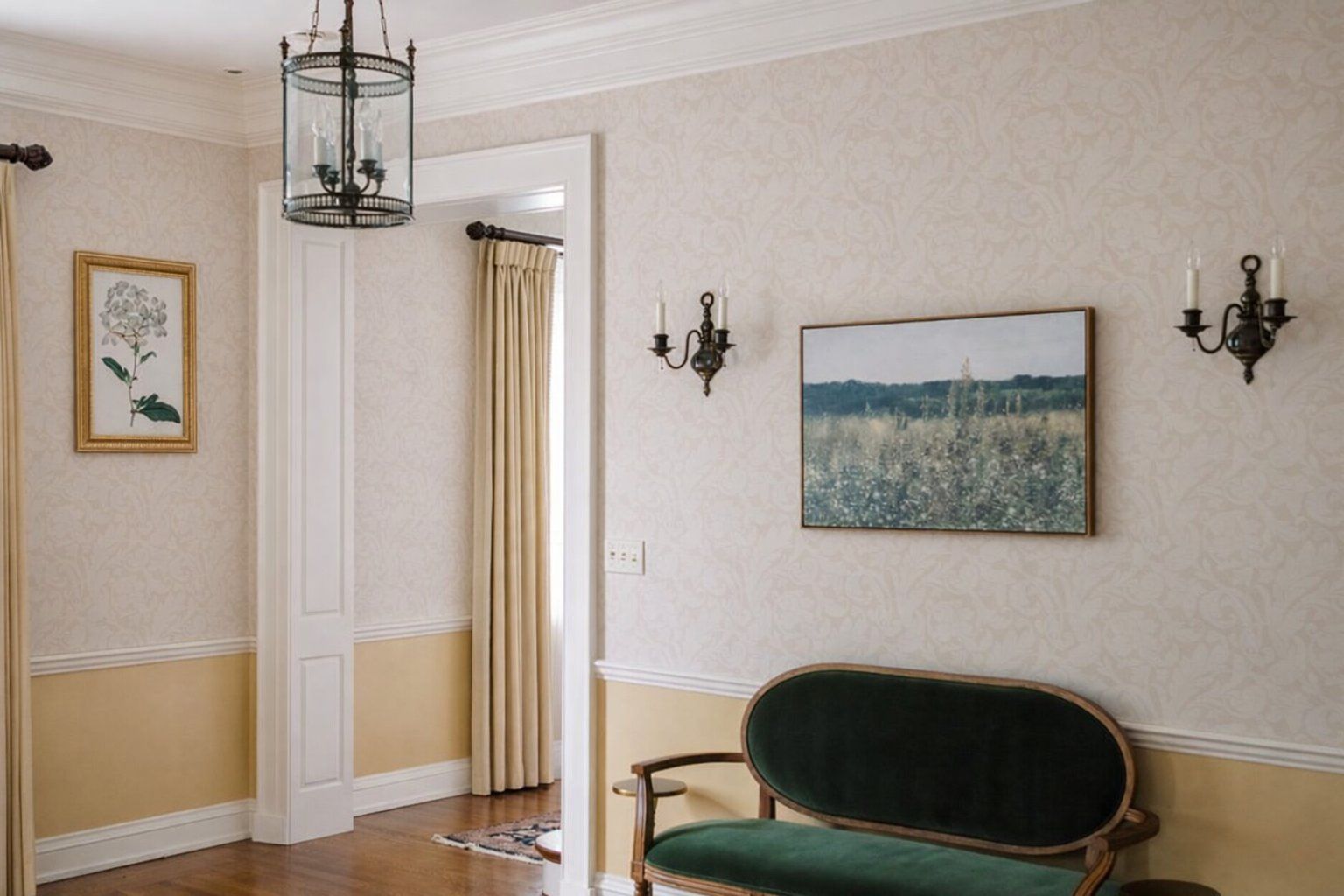 A hallway with a green upholstered bench, a framed floral painting, a landscape painting, and wall sconces.