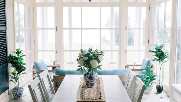 A conservatory with a dining table, chairs, and potted plants.