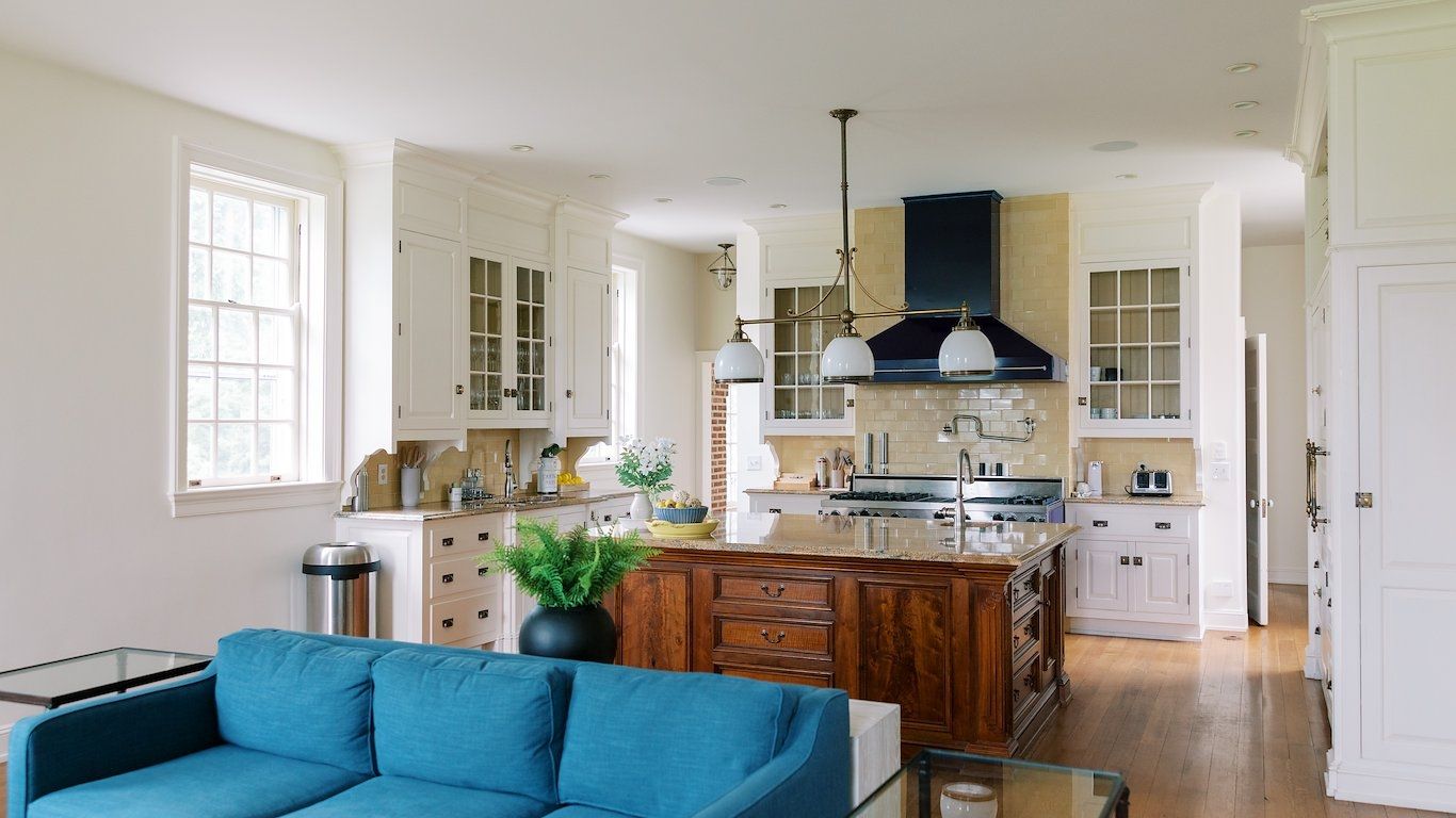 A spacious kitchen with white cabinetry, a central island, and a blue sofa in the living area.