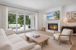 A modern living room with a fireplace, a sofa, a coffee table, and a view of the outdoors.