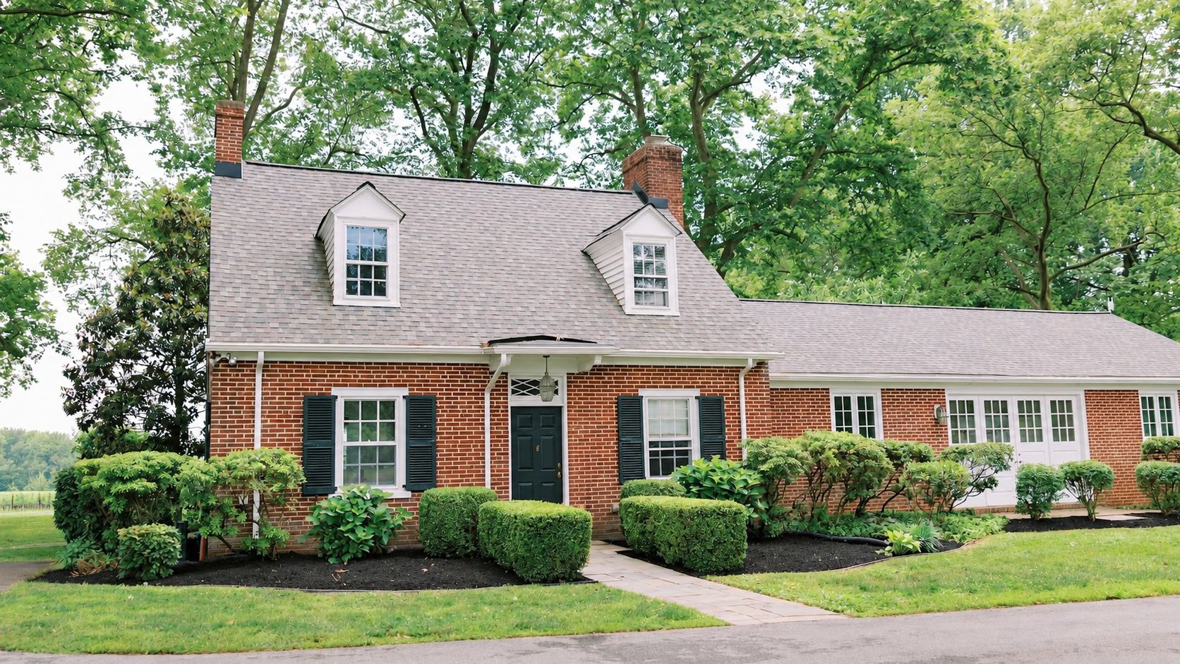 A two-story brick house with a front porch, a chimney, and a well-maintained lawn.