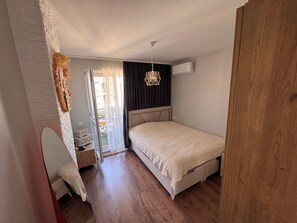 A bedroom with a bed, a bedside table, a chair, a wardrobe, and a sliding glass door leading to a balcony.