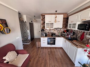 Una cocina compacta con armarios blancos, horno empotrado y microondas.