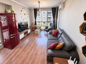 Una sala moderna con sofá, televisor, mesa de comedor y refrigerador.