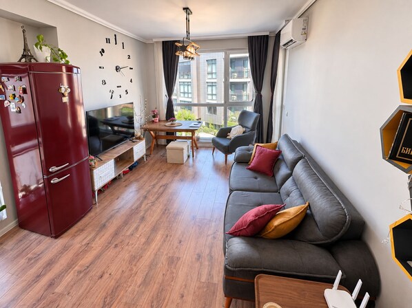 A modern living room with a sofa, a television, a dining table, and a refrigerator.