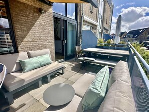 Eine Außenpatio mit einer Couch, einem runden Tisch und einem Esstisch mit Stühlen.