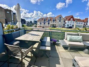 Eine Außenpatio mit Tisch und Stühlen, eine Sitzecke mit Kissen und Blick auf Wohnhäuser im Hintergrund.