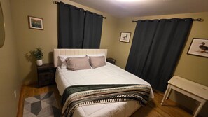 A bedroom with a bed, curtains, a bedside table, a nightstand, a floor lamp, a small table, and a wall-mounted picture. - COMING SOON! Enjoy Montana all year round, 5 bedrooms for your get away!  (Gallatin Gateway)
