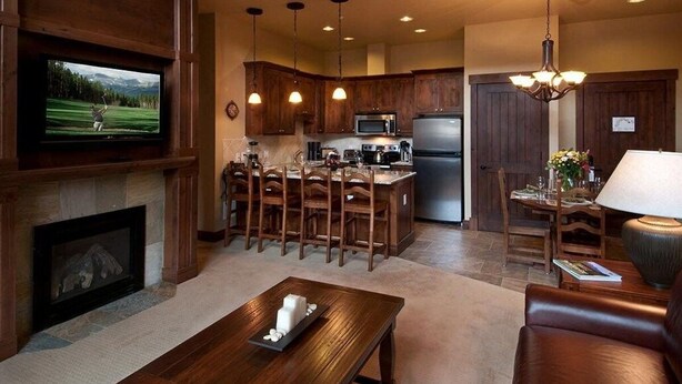 Amplia sala de estar con chimenea, televisor, comedor con sillas de madera y cocina equipada con refrigerador y microondas.