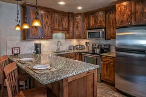 Una cucina con mobili in legno, piani di lavoro in granito, elettrodomestici in acciaio inossidabile e luci a sospensione.