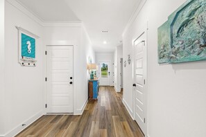 A hallway with white walls, wooden flooring, and a door at the end leading to a room. - Dama Oasis - Luxurious Home W/ Private Pool! (Panama City Beach)