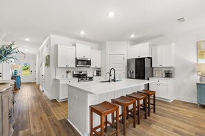 Une cuisine moderne avec des meubles blancs, un îlot central doté de tabourets, des appareils en acier inoxydable et un plancher en bois.