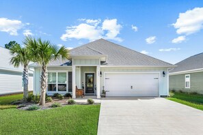A single-story house with a front garage, a small porch with a bench, and a palm tree in the front yard. - Dama Oasis - Luxurious Home W/ Private Pool! (Panama City Beach)