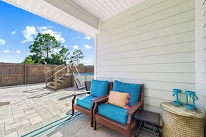 A covered patio with a wooden bench, a small table, and a woven stool. - Dama Oasis - Luxurious Home W/ Private Pool! (Panama City Beach)