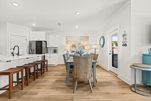 A modern kitchen with white cabinetry, a stainless steel refrigerator, and wooden bar stools. - Dama Oasis - Luxurious Home W/ Private Pool! (Panama City Beach)