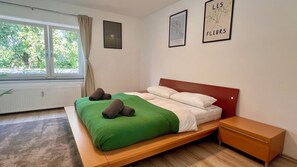 A bedroom with a bed, a nightstand, a window, and two wall art pieces.
