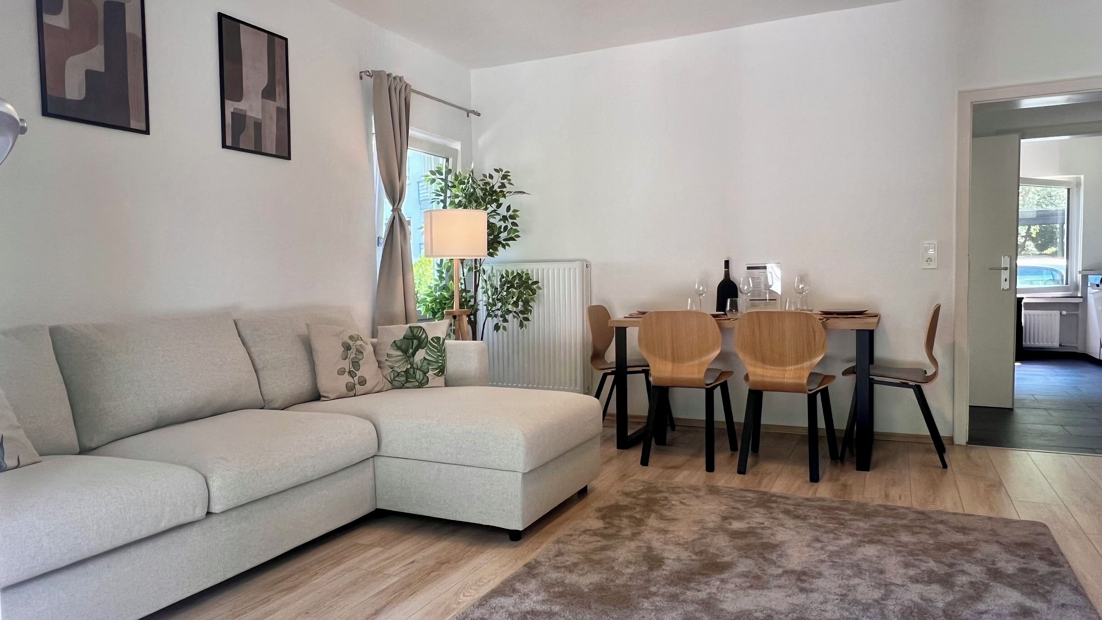 Ein modernes Wohnzimmer mit einer Couch, einem Esstisch mit Stühlen, einer Heizung und einem Fenster mit Vorhängen.