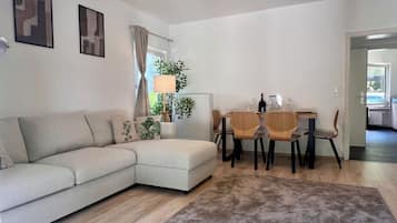 Ein modernes Wohnzimmer mit einer Couch, einem Esstisch mit Stühlen, einer Heizung und einem Fenster mit Vorhängen.