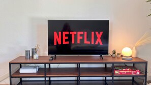 A television with the Netflix logo on a wooden stand with a shelf below.