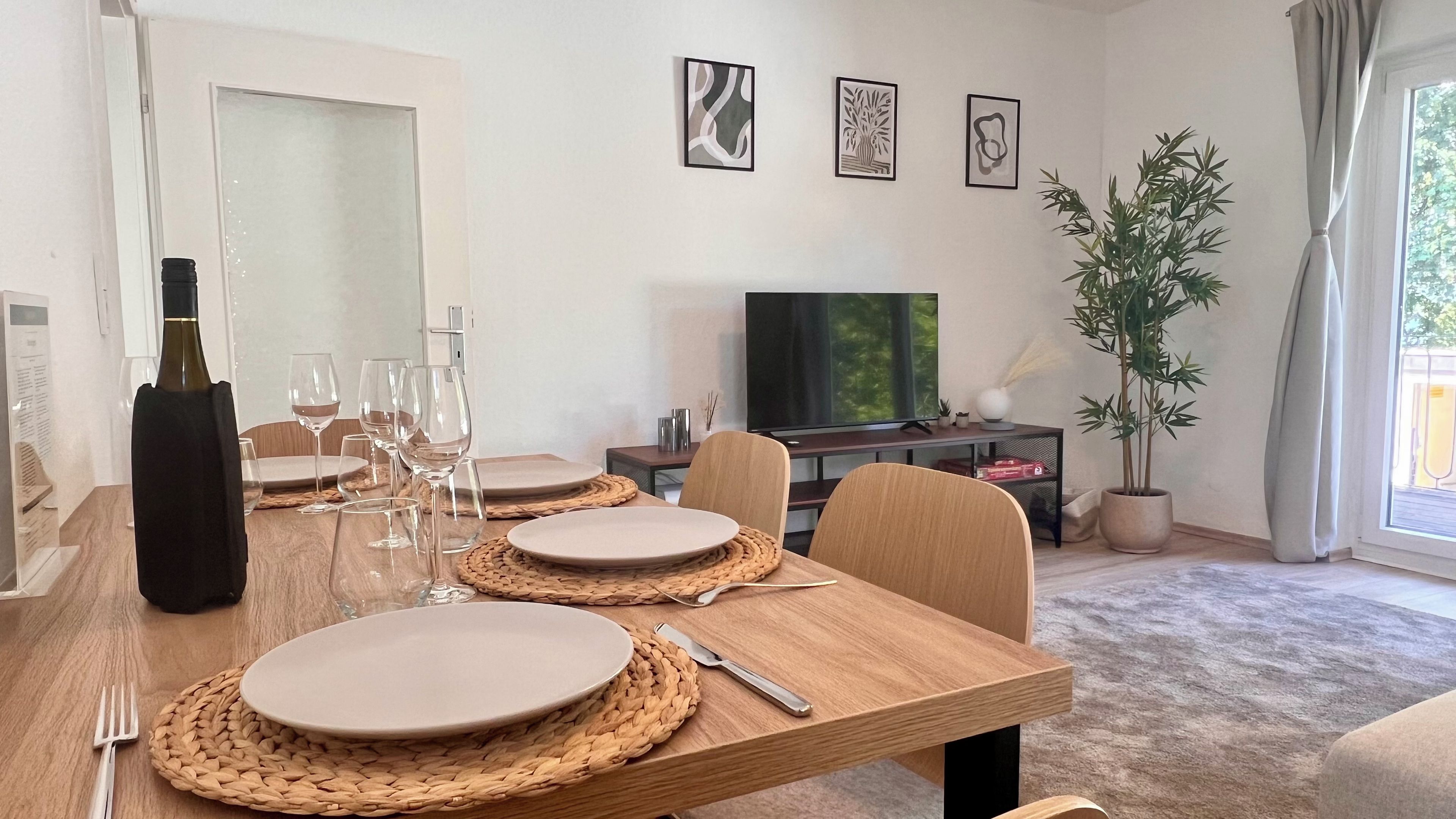 Ein Essbereich mit einem Holztisch, gedeckt für vier Personen, einem Fernseher und gerahmten Kunstwerken an der Wand.