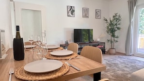 A dining area with a wooden table set for four, a television, and framed artwork on the wall.